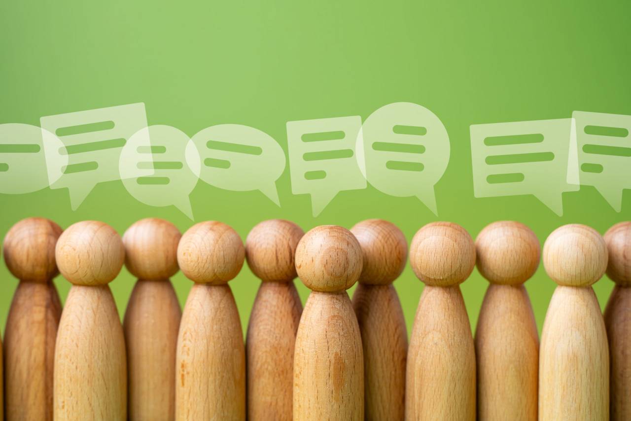 Row of wooden peg dolls with white speech bubbles above their heads on a green background